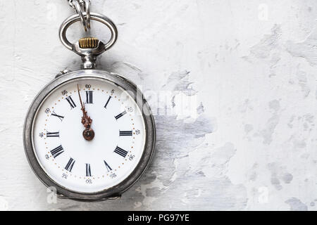 two minutes to twelve o'clock on vintage pocket watch on white concrete background Stock Photo