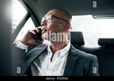 Businessman wearing eyeglasses talking over cell phone sitting in his sedan looking out the window. Man managing business on mobile phone sitting in c Stock Photo