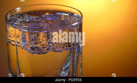 Glass with soda water and ice cubes with bubbles on a bright background. Close up view Stock Photo