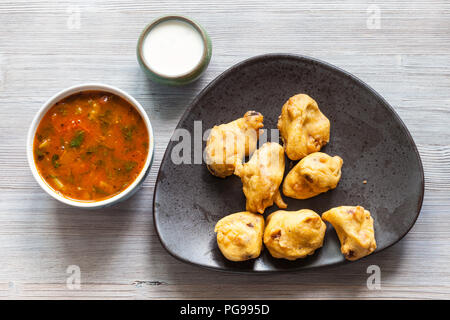 Indian cuisine - Chicken Pakoda pieces dipped in spiced butter on black plate served with sambar and chutney sauces on gray wooden table Stock Photo