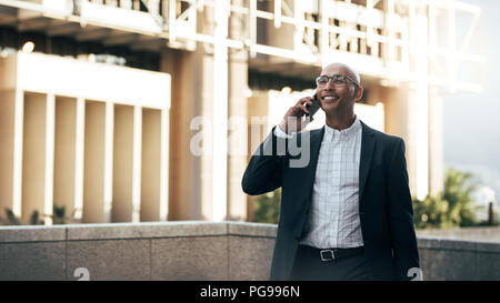 Smiling businessman talking over cell phone standing on terrace of a building. Man in formal clothes standing on a building talking on mobile phone. Stock Photo