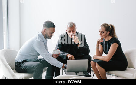 Male executive viewing proposal on laptop to his colleagues in office foyer. Group of three business professionals working together on new business pl Stock Photo