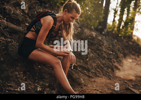 Fit woman checking progress on smart watch during trail run break. Female runner sitting by mountain trail and looking at smart watch heart rate monit Stock Photo