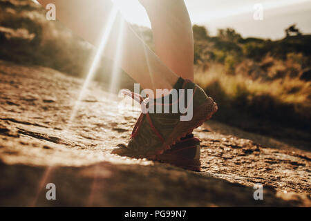 Close up female mountain trail runner wearing sports shoe standing in sunlight. Woman in running shoes standing in rocky trail. Stock Photo