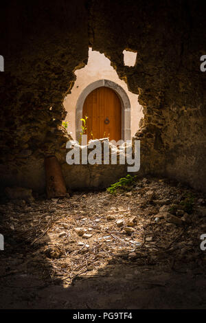 An old wooden arched door in Sicily seen through a broken hole in a stone wall Stock Photo