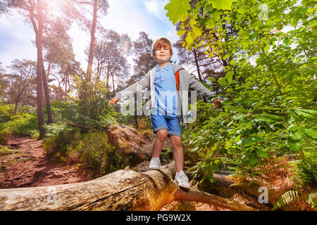 Small boy walks over log in forest with backpack Stock Photo