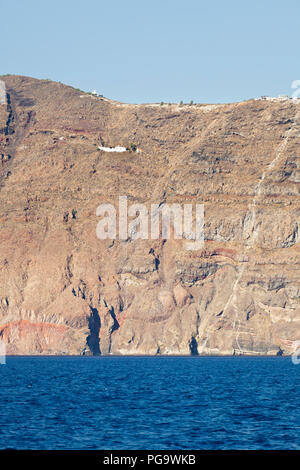 View from a boat to the tall cliffs of Santorini, Greece with a chapel in the wall. Stock Photo