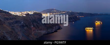 View from Imerovigli along the crater rim to Fira with two illuminated cruise ships lying in the water of Santorini, Greece. Stock Photo