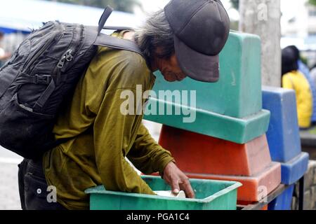 Antipolo City, Philippines - August 18, 2018: A scavenger goes through trash bins to look for recyclable materials. Stock Photo