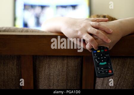 Photo of a woman sitting on a couch holding a remote control. Stock Photo