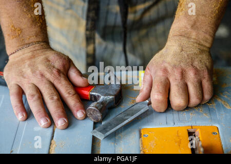 Man's hands covered in saw dust with hammer and a chisel on a table saw . Carpentry tools, concept of wood work. Stock Photo