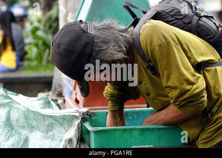 Antipolo City, Philippines - August 18, 2018: A scavenger goes through trash bins to look for recyclable materials. Stock Photo