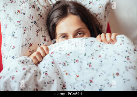 Young girl look under blanket in her bed, closeup. Beautiful woman hiding face Stock Photo