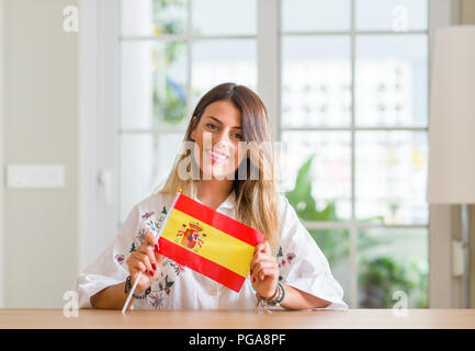 Young woman at home holding flag of Spain with a happy face standing and smiling with a confident smile showing teeth Stock Photo