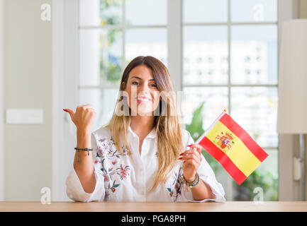 Young woman at home holding flag of Spain pointing with hand and finger up with happy face smiling Stock Photo