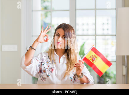 Young woman at home holding flag of Spain doing ok sign with fingers, excellent symbol Stock Photo