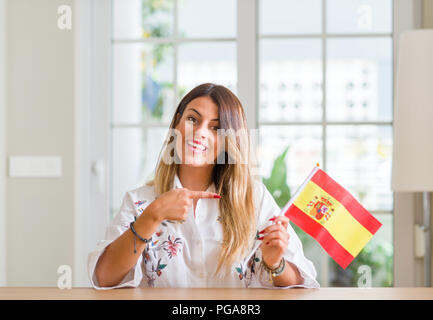 Young woman at home holding flag of Spain very happy pointing with hand and finger Stock Photo