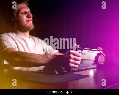 young mad crazy gamer breaking the keyboard playing video games on computer late in the night Stock Photo