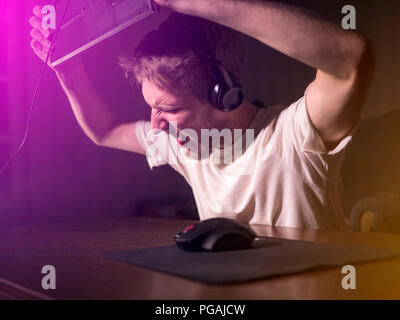 young mad crazy gamer breaking the keyboard playing video games on computer late in the night Stock Photo