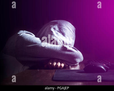 abstract anonymous person in the hood sleeping lying on the table in front of computer in the night Stock Photo