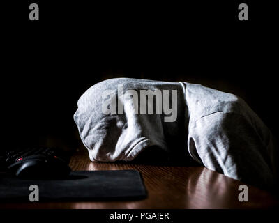 abstract anonymous person in the hood sleeping lying on the table in front of computer in the night Stock Photo