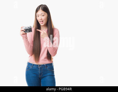 Young Chinese woman over isolated background taking pictures using vintage camera very happy pointing with hand and finger Stock Photo