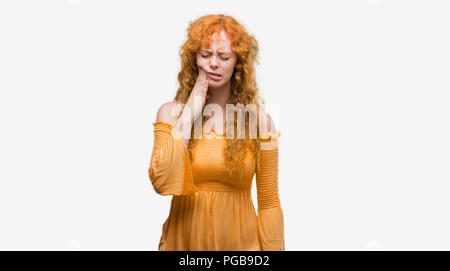 Young redhead woman touching mouth with hand with painful expression because of toothache or dental illness on teeth. Dentist concept. Stock Photo