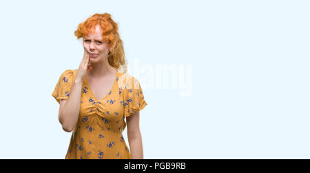 Young redhead woman touching mouth with hand with painful expression because of toothache or dental illness on teeth. Dentist concept. Stock Photo