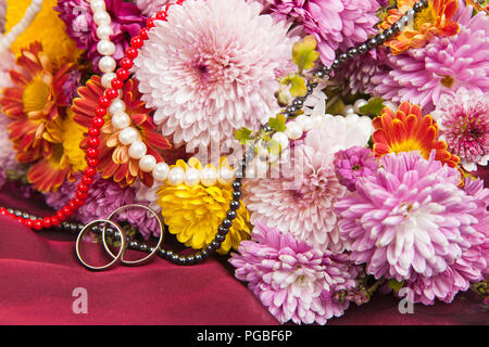 Colorful chrysanthemum and daisy flowers on a claret fabric with wedding rings and a beads Stock Photo