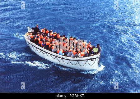 1970s, historical, cruise passengers with orange coloured life jackets, out at sea on a lifeboat taking part in a ship's life safety drill. Stock Photo