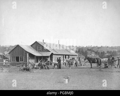 Farm equipment, horses, wagons, dogs, cowboys and others posed in front of western ranch houses Stock Photo