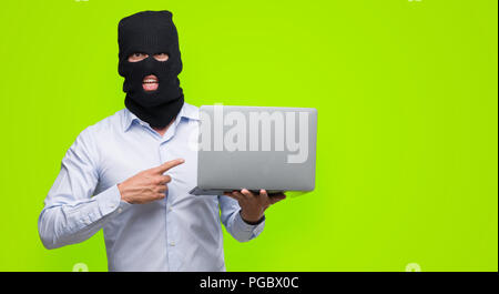 Business hacker man holding a computer laptop very happy pointing with hand and finger Stock Photo