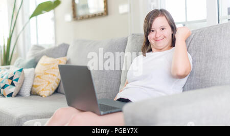 Down syndrome woman at home using computer laptop screaming proud and celebrating victory and success very excited, cheering emotion Stock Photo