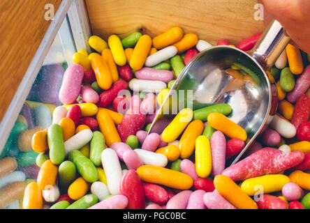 Close-up of multi-colored candy sticks / sweets with a hand filling a scoop from a wooden box Stock Photo