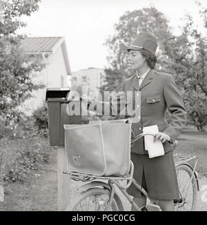 1960s postman. A woman in the swedish postal service uniform delivers mail and put the letters in a mailbox. Sweden 1960s.  Photo Kristoffersson DG114-7 Stock Photo