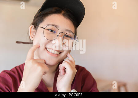 Chubby plump teen cute white tooth smile Asian young student with glasses and hat finger touch cheek with copy space Stock Photo