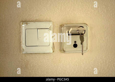 Classic mechanic key with card in slot to activate electricity in hotel room. Old dirty wall and socket. Stock Photo