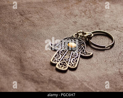 A key ring in the form of Fatima Hand on a brown leather background. Ancient symbol and traditional modern tourist souvenir of Tunisia. Stock Photo