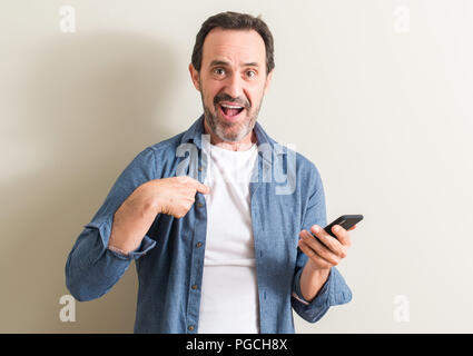 Senior man using smartphone with surprise face pointing finger to himself Stock Photo