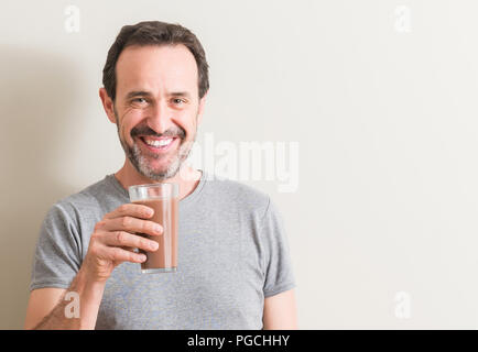 Senior man drinking chocolate milk shake with a happy face standing and smiling with a confident smile showing teeth Stock Photo