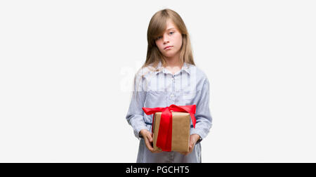 Young blonde toddler holding a present with a confident expression on smart face thinking serious Stock Photo