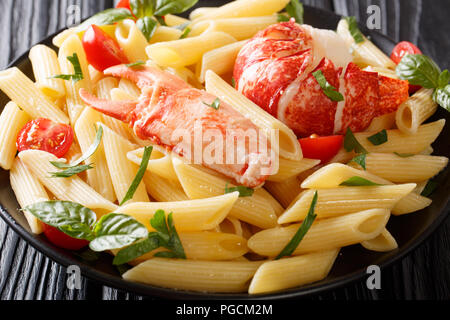 Delicious food: penne pasta with seafood lobster meat, tomatoes and herbs close-up on a plate on the table. horizontal Stock Photo