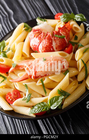 Penne pasta with lobster meat, tomatoes and herbs close-up on a plate on a table. vertical Stock Photo