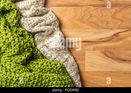 Wool blanket, white and green, knitted large chunky yarn. Close-up of knitted blankets on wooden background. Stock Photo