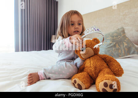 Innocent young girl putting a crown on her teddy bear. Little girl playing with her soft toy. Stock Photo