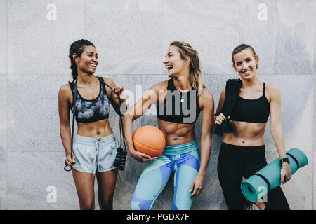 Happy women in fitness clothes relaxing and having fun standing against a wall. fitness women carrying skipping rope basketball and workout mat standi Stock Photo