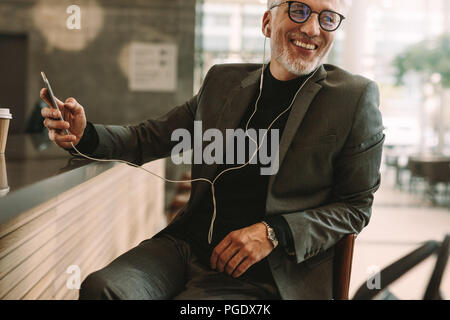 Handsome mature man sitting at coffee shop listening music for mobile phone. Business man sitting in front of cafe counter enjoying listening music ov Stock Photo