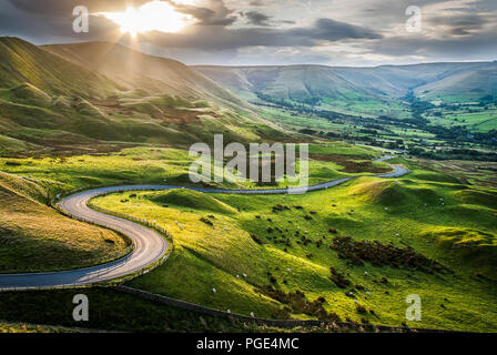 Sunset at Mam Tor, Peak District National Park, with a view along the winding road down to Hope Valey, in Derbyshire, England. Flock of sheep grazing. Stock Photo