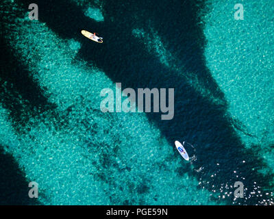 Aerial view of two people doing stand up paddleboarding (SUP) on a beautiful turquoise sea. Cala Brandinchi, Sardinia, Italy. Stock Photo