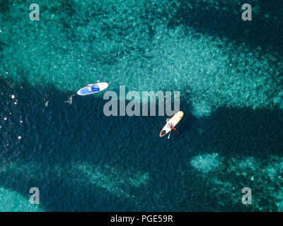 Aerial view of two people doing stand up paddleboarding (SUP) on a beautiful turquoise sea. Cala Brandinchi, Sardinia, Italy. Stock Photo